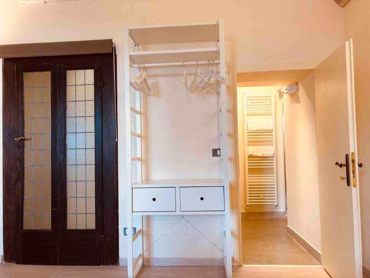 Una stanza con una porta in legno scuro, un'armadio bianco con spazio per appendere e una piccola scrivania con cassetti.