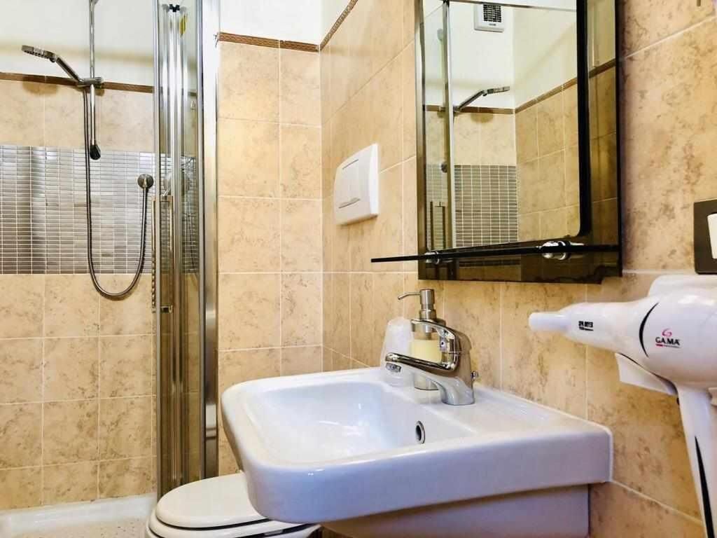 A bathroom with a glass-enclosed shower, a white sink with a soap dispenser, and a hairdryer on the right.