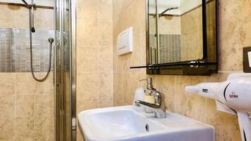A bathroom with a glass-enclosed shower, a white sink with a soap dispenser, and a hairdryer on the right.