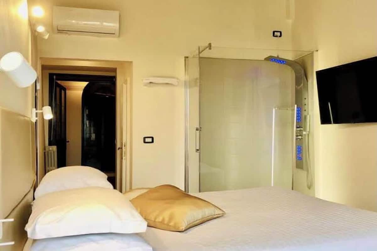 Ett hotellrum med en säng, en tv som är monterad på väggen och en duschhörna.