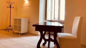 A room with a dark wooden table, a white chair, a white cabinet, and a floor lamp. - Mavitur Rooms (Assisi)