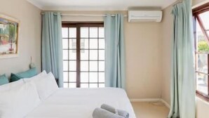 A hotel room with a bed, a window with curtains, an air conditioning unit, and a painting on the wall. - Nansen Place (Cape Town)