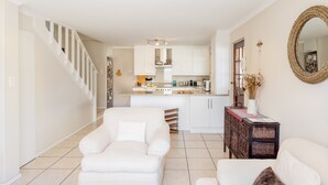 A spacious living area with a white sofa, a small side table, and a staircase leading to a kitchen area. - Nansen Place (Cape Town)