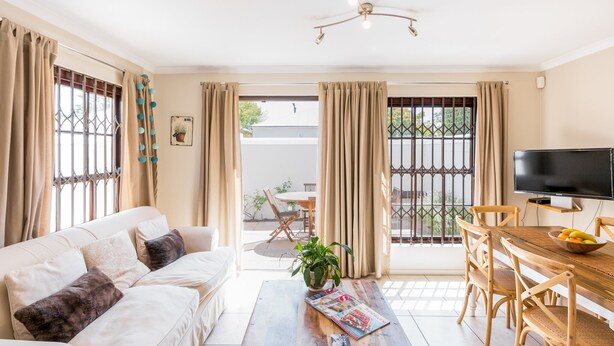 A living room with a sofa, coffee table, and TV. There is a dining area with a table and chairs. - Nansen Place (Cape Town)