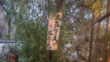An outdoor seating area with a table and chairs, surrounded by greenery and a hanging banner with Chinese characters.