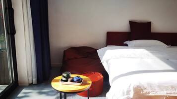 A hotel room with a bed, a small table with a tray of items, a red chair, and a window with curtains.