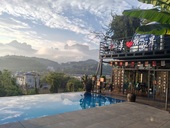 A pool with a view of mountains, a restaurant with outdoor seating, and a sign with Chinese characters.