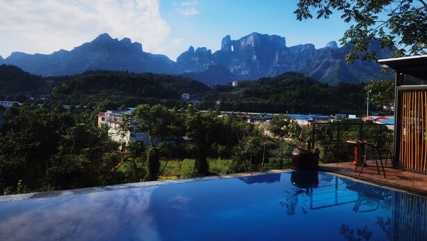 Une piscine avec vue sur les montagnes, entourée de verdure et bordée d’une structure en bois.