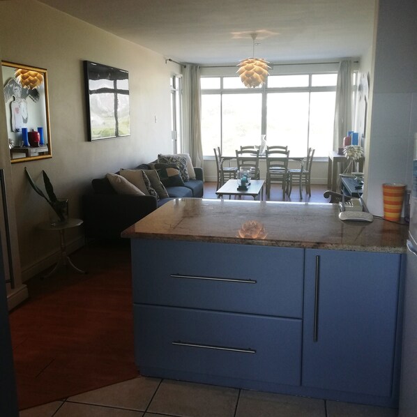 A modern kitchen with a blue island, a dining area with a table and chairs, and a living area with a sofa and a coffee table. - Villa Marina (Cape Town)