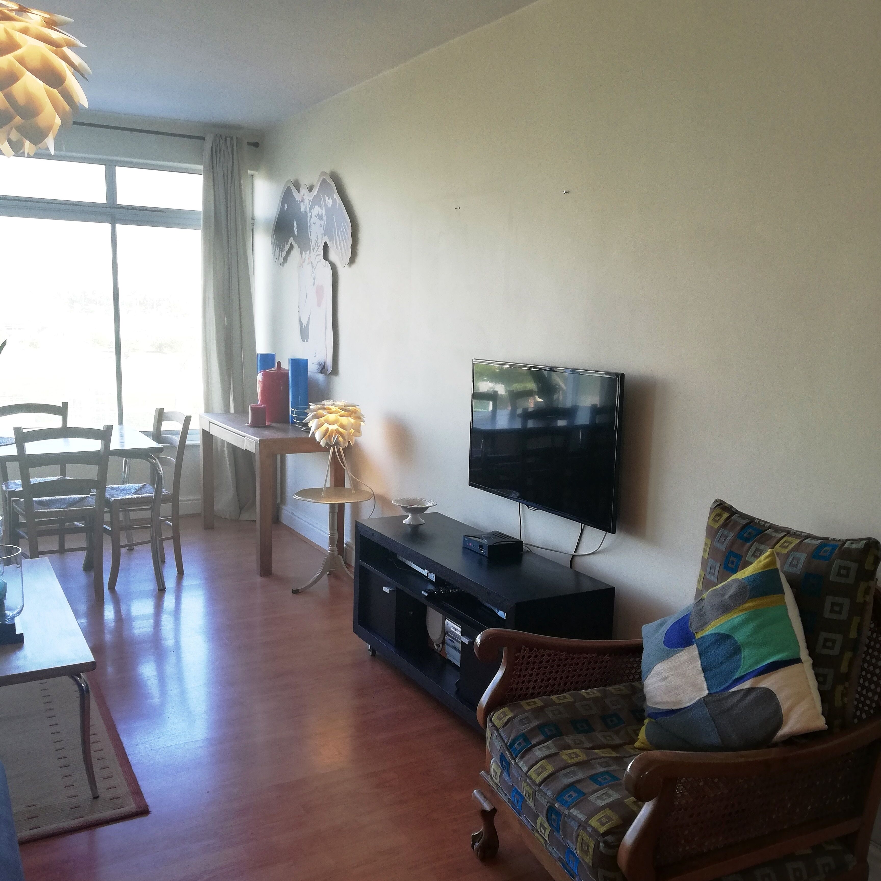 A living room with a TV, wooden furniture, a dining table, and a large window.