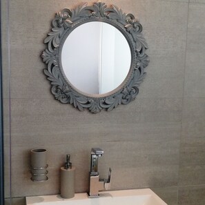 A bathroom with a round mirror, a sink, and a toilet. - Villa Marina (Cape Town)