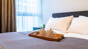 Een net opgemaakt bed met witte kussens en een houten dienblad met twee witte mokken.