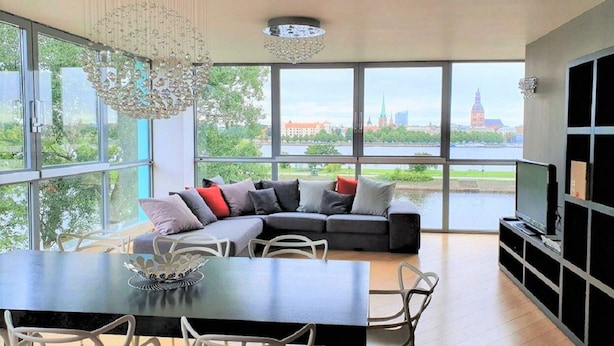 Een moderne woonkamer met een groot raam, een hoekbank, een eettafel en een televisie.