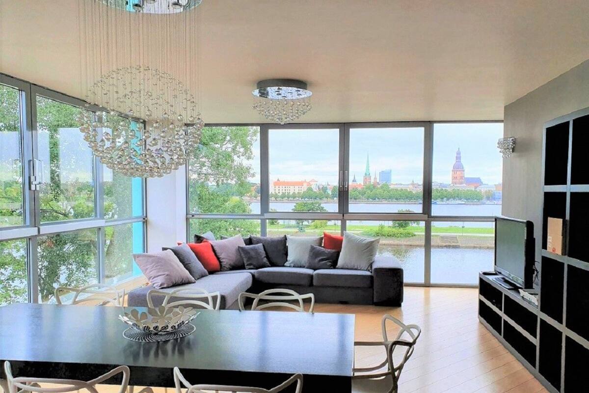 Una sala de estar moderna con un ventanal grande, un sofá modular, una mesa de comedor y un televisor.