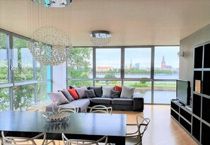 Una sala de estar moderna con un ventanal grande, un sofá modular, una mesa de comedor y un televisor.