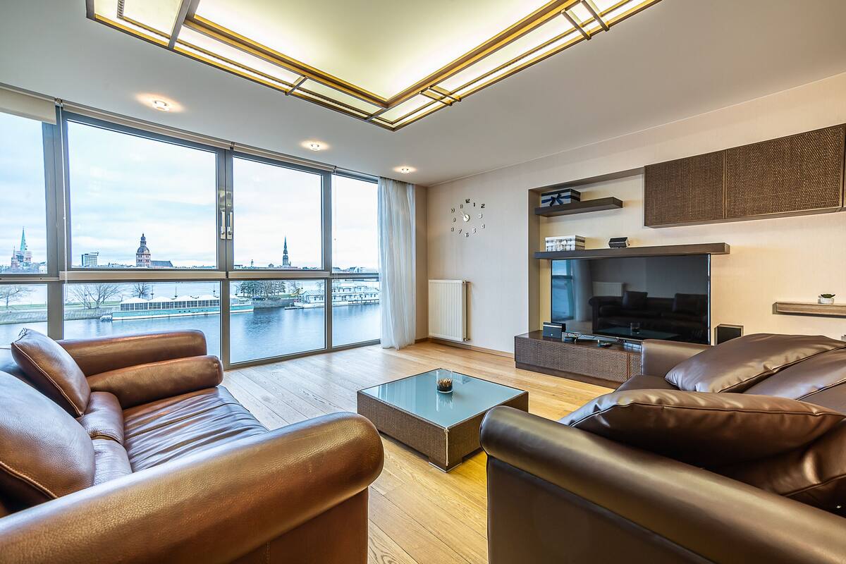 Una sala de estar moderna con sofás de cuero, una mesa de centro de vidrio y un televisor grande.