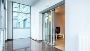 Een moderne hotelgang met een grote glazen deur naar een kamer met een houten vloer en een bed.