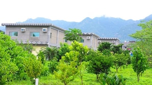 Un quartier résidentiel où les maisons présentent un style architectural uniforme, entouré d’une végétation luxuriante et avec des montagnes en toile de fond.