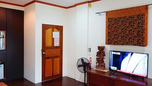 Une pièce avec une porte en bois, un ventilateur fixé au mur, un téléviseur à écran plat et un élément décoratif mural.
