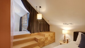 A bedroom with a wooden staircase, a bed with white bedding, a nightstand with a lamp, and a window with curtains.