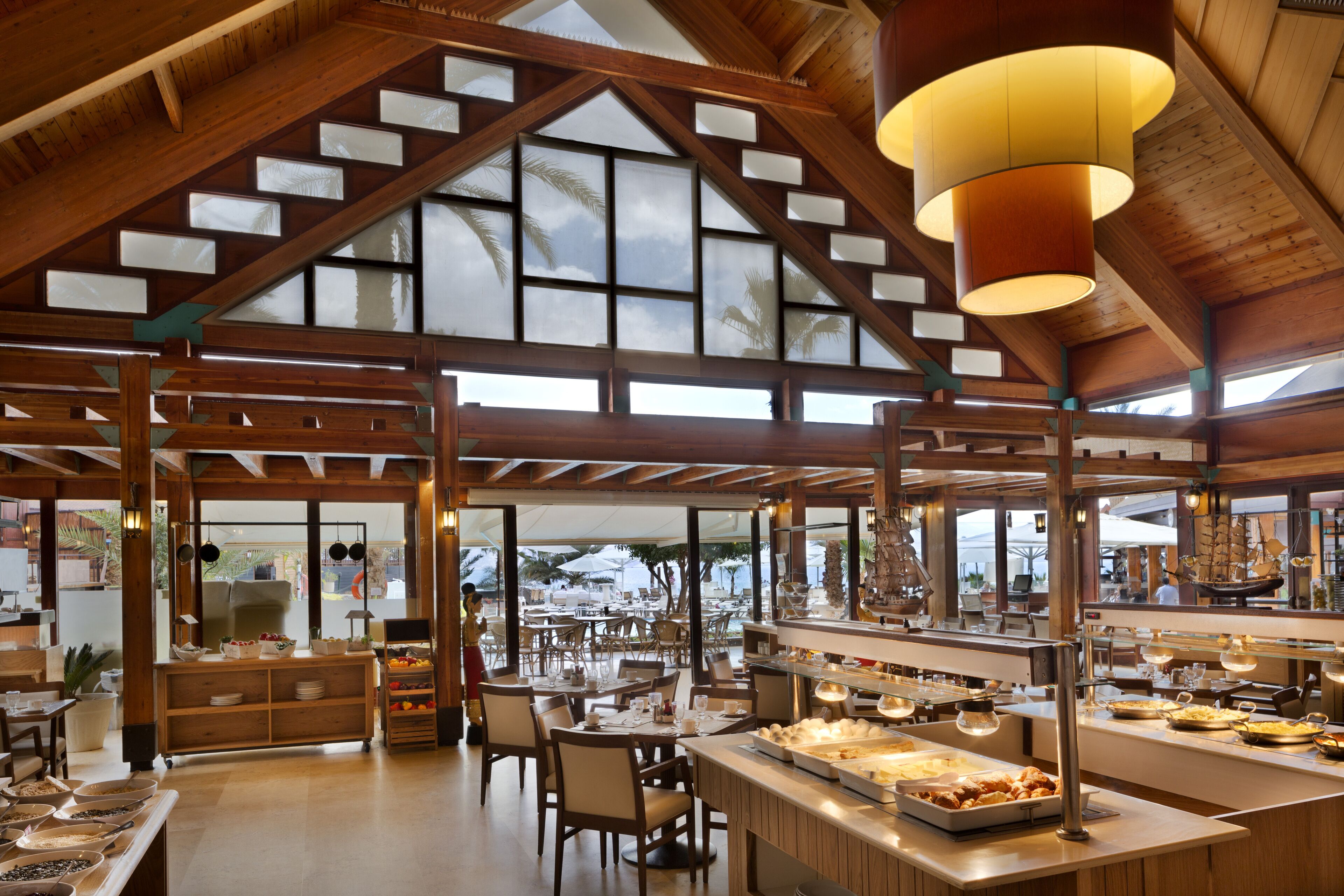 Un restaurante espacioso con techos altos, vigas de madera y amplios ventanales que ofrecen vistas al exterior.