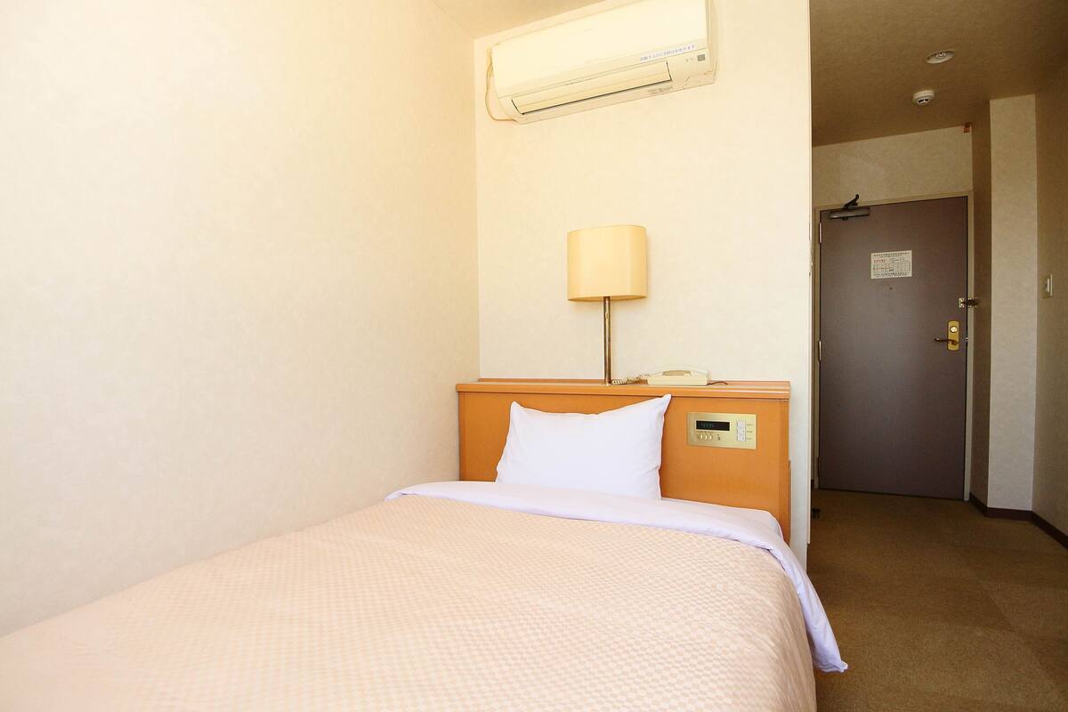 A hotel room with a bed, a nightstand, a lamp, and a door.