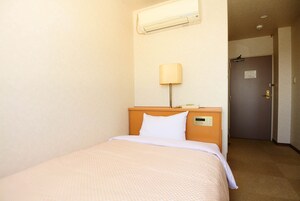Una habitación de hotel con cama, mesita de noche, lámpara y puerta.