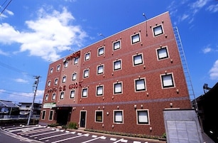 Un edificio de varios pisos de ladrillo, con una hilera de ventanas en cada nivel, una entrada visible y un cielo despejado al fondo.