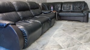 A modern living room with a black leather sofa and a smaller armchair, a tiled floor, and a framed picture on the wall. - Peemens Guesthouse (Ngleshi Amanfro)