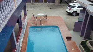 A rectangular pool with a blue interior, surrounded by a tiled deck. There are two white tables and four chairs on the deck. - Peemens Guesthouse (Ngleshi Amanfro)