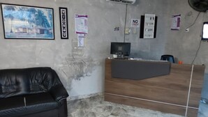 A reception area with a wooden desk, a black leather couch, and a tiled floor. - Peemens Guesthouse (Ngleshi Amanfro)