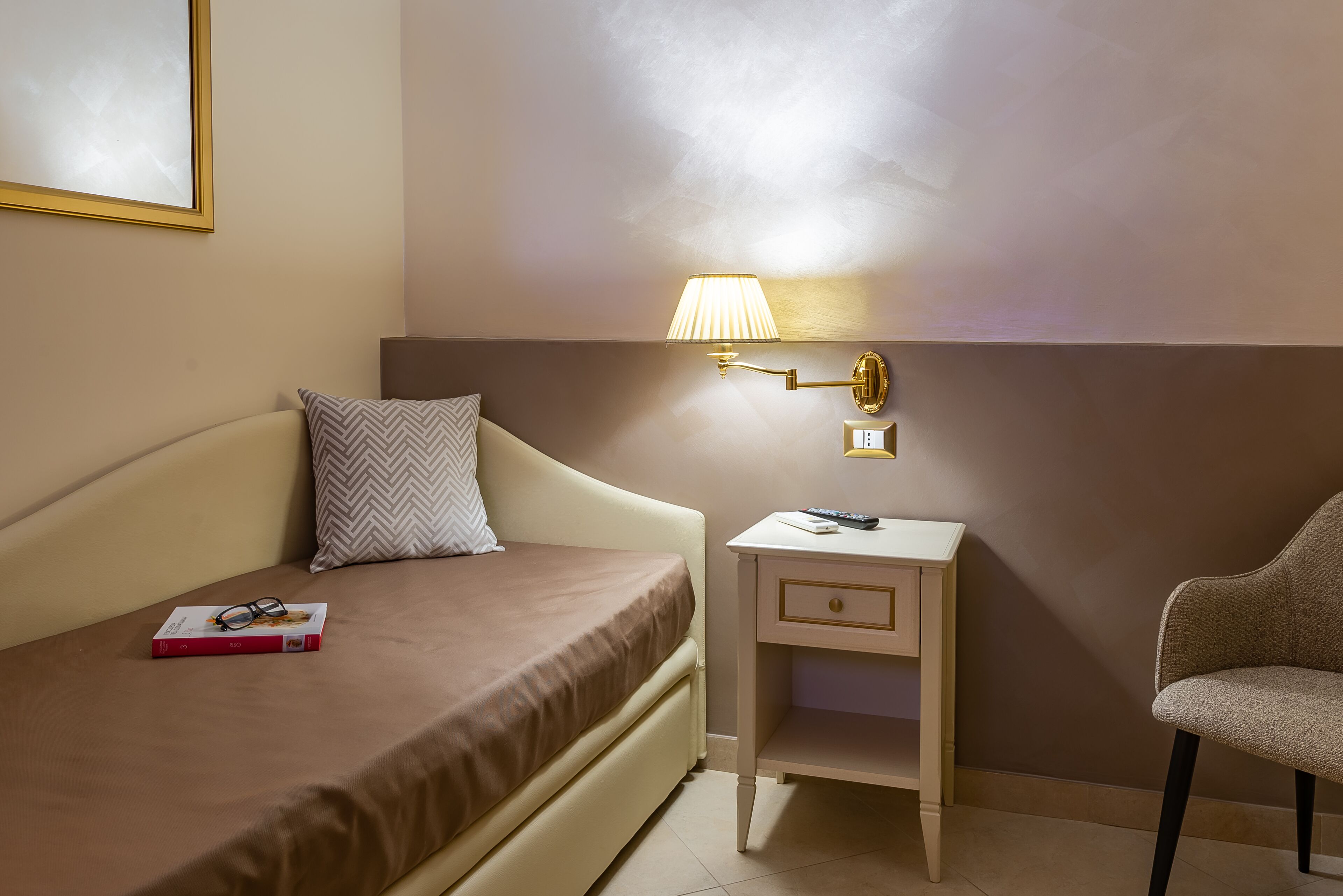Ein Hotelzimmer mit Bett, Nachttisch, Lampe, Stuhl und einem gerahmten Bild an der Wand.