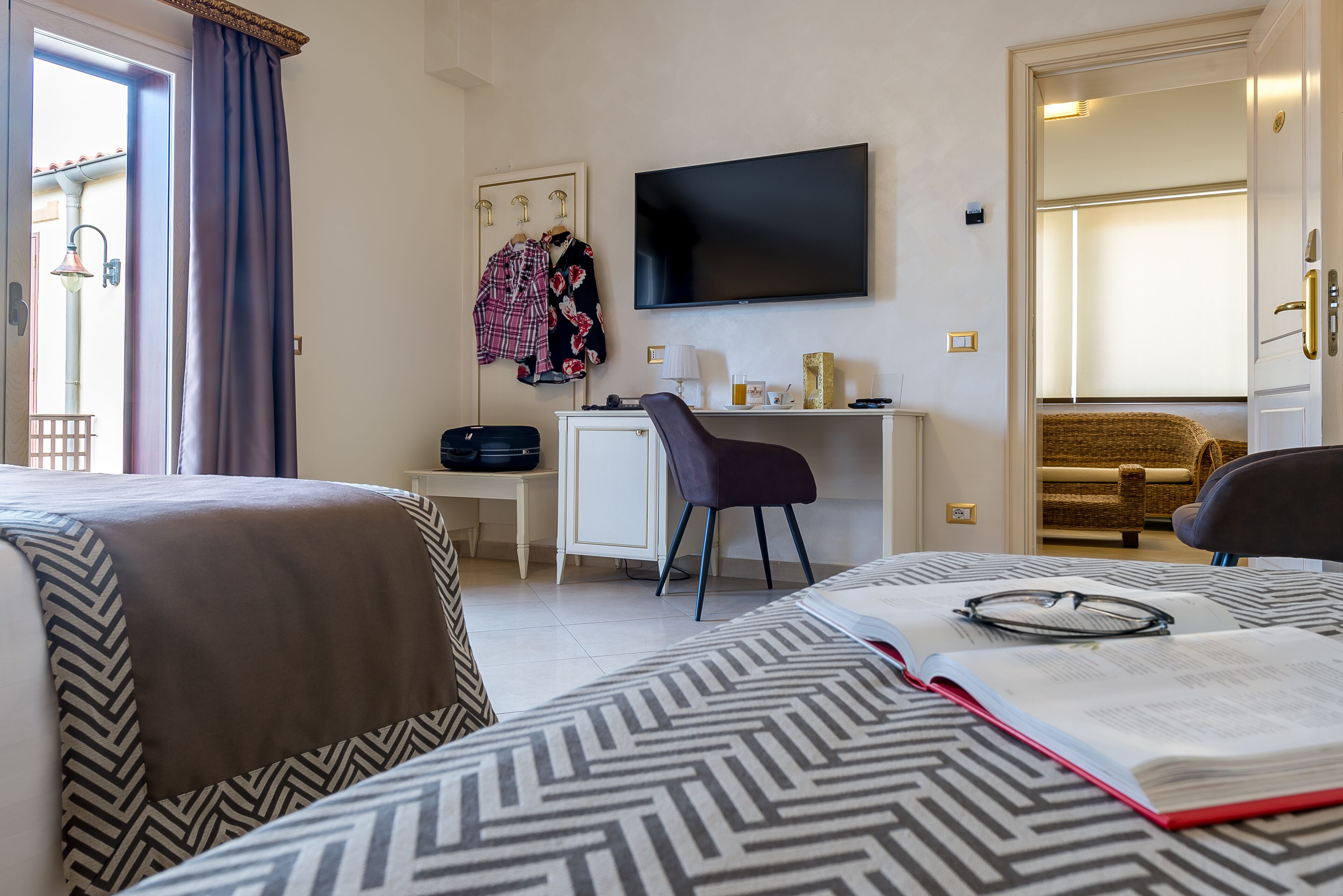 A hotel room with two beds, a desk, a chair, a television, and a window with curtains.