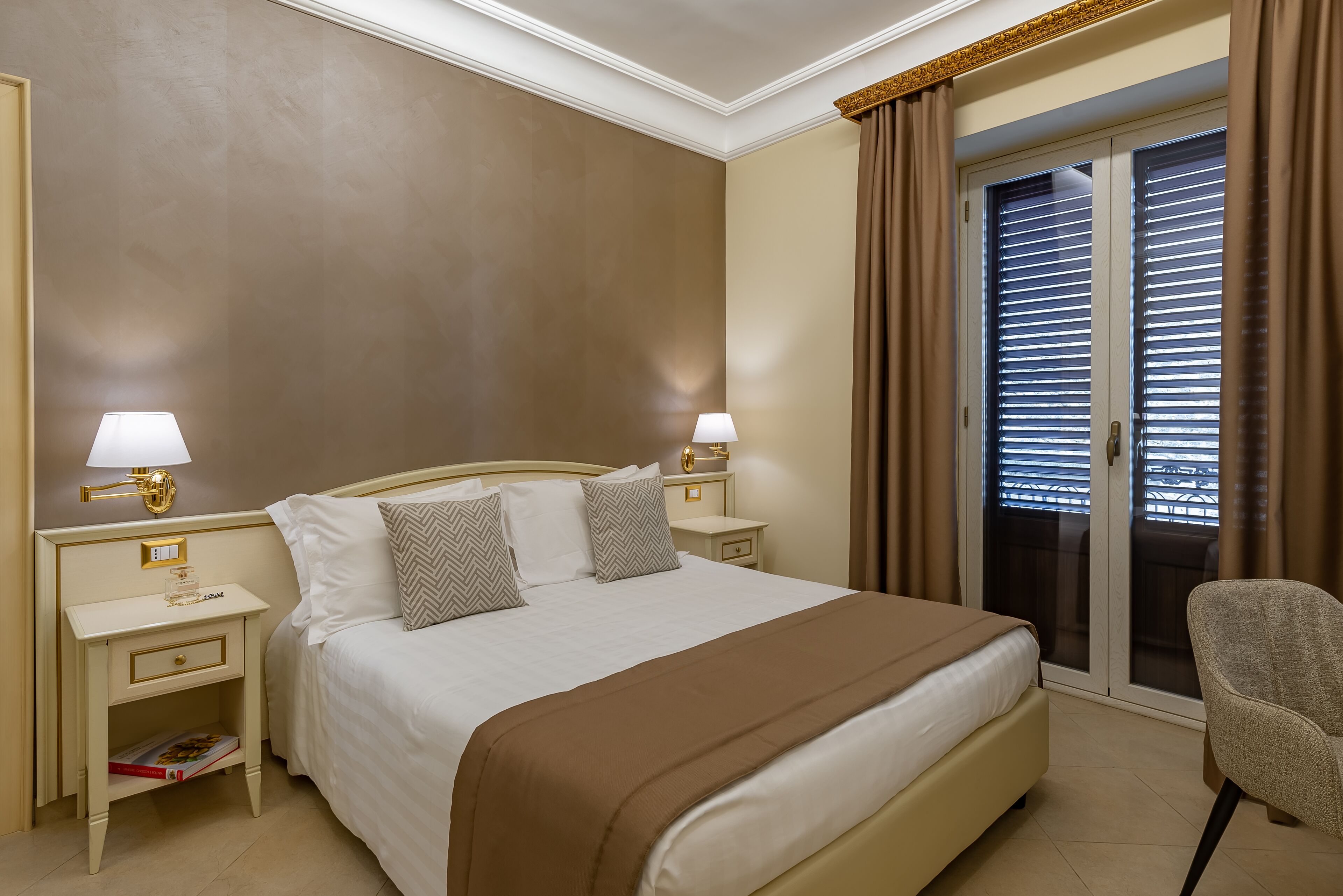 A hotel room with a large bed, two bedside tables with lamps, a chair, and a sliding glass door to the balcony.