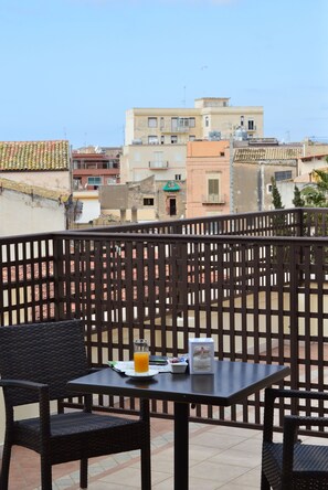 A balcony with wicker chairs and a table, a glass of orange juice, and a menu. - Vittorio Emanuele Boutique Hotel (Sciacca)