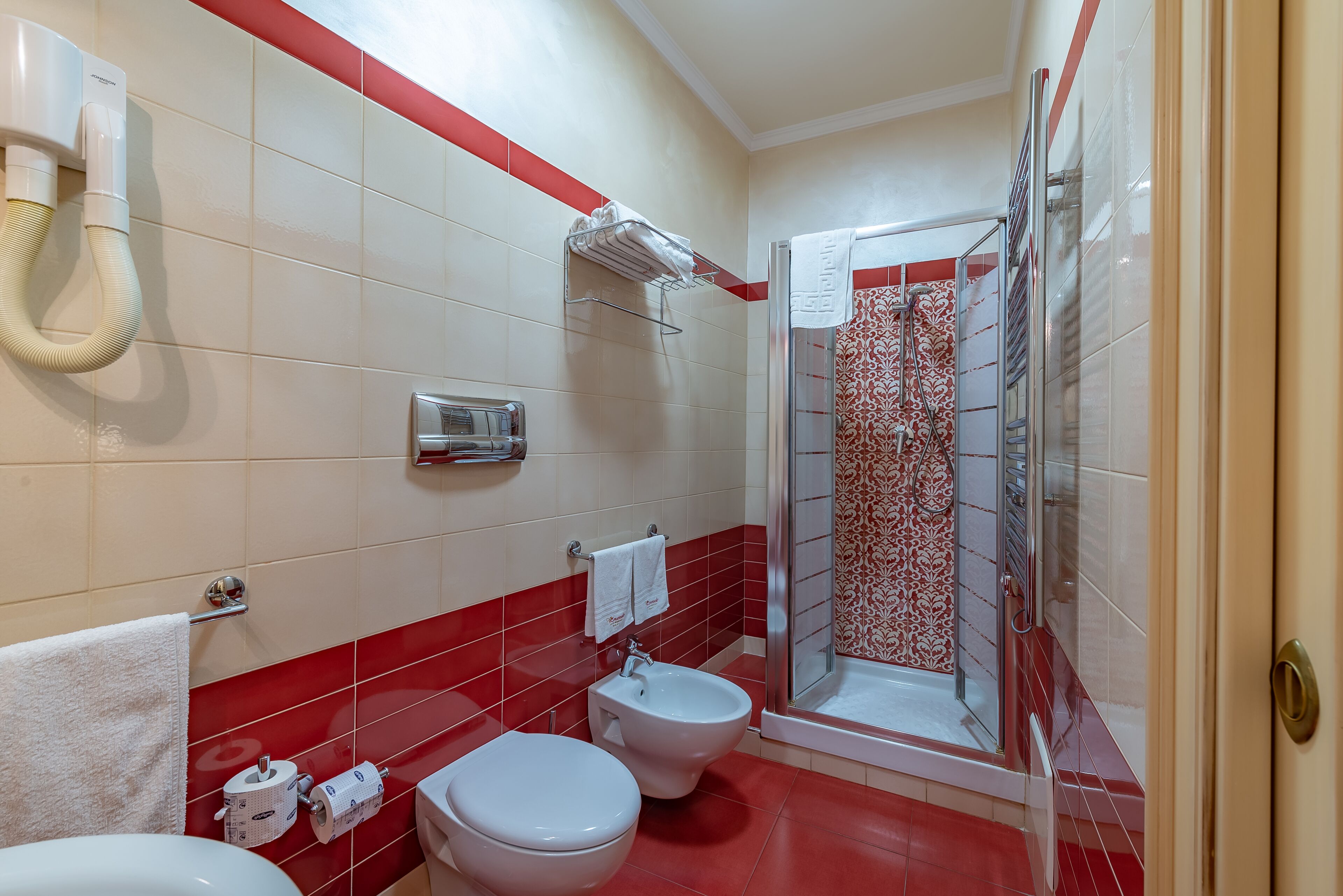 Un baño con dos inodoros, un bidé, un perchero para toallas y una ducha con puerta de cristal.