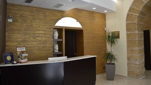A reception area with a wooden wall, a reception desk, a large potted plant, and a stone archway. - Vittorio Emanuele Boutique Hotel (Sciacca)