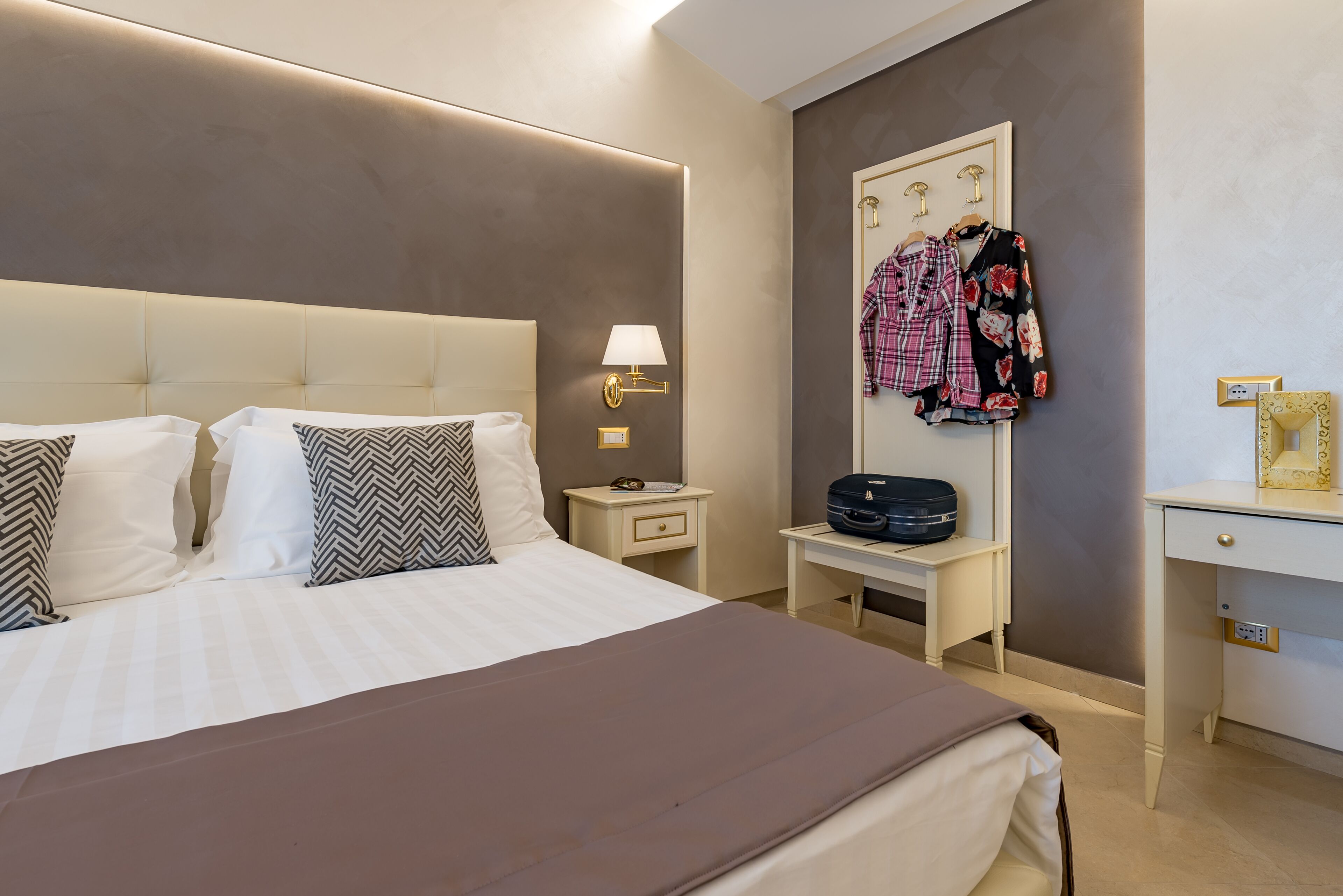 Habitación de hotel con una cama grande, una mesita de noche con lámpara, un armario y un escritorio con una maleta.