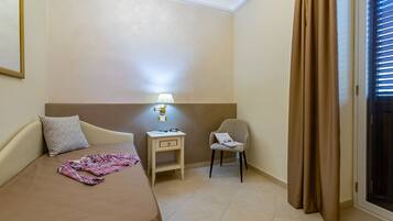 Habitación de hotel con cama, mesita de noche, lámpara, silla y cortinas.