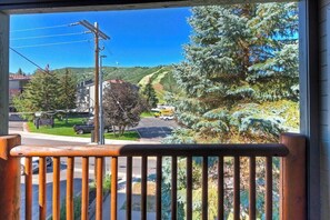 A view from a balcony overlooking a road with a building and trees in the background.