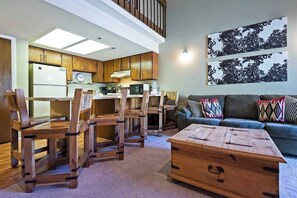 A modern kitchen with wooden cabinets, a dining area with wooden chairs, a sofa, and a coffee table.