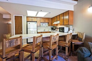 A modern kitchen with wooden cabinets, a central island with bar stools, and a built-in microwave.