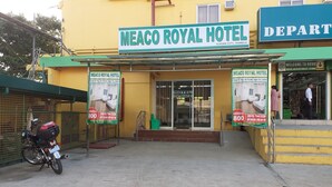 La façade de l’hôtel Meaco Royal, avec son panneau indicateur, son entrée et une moto garée devant.