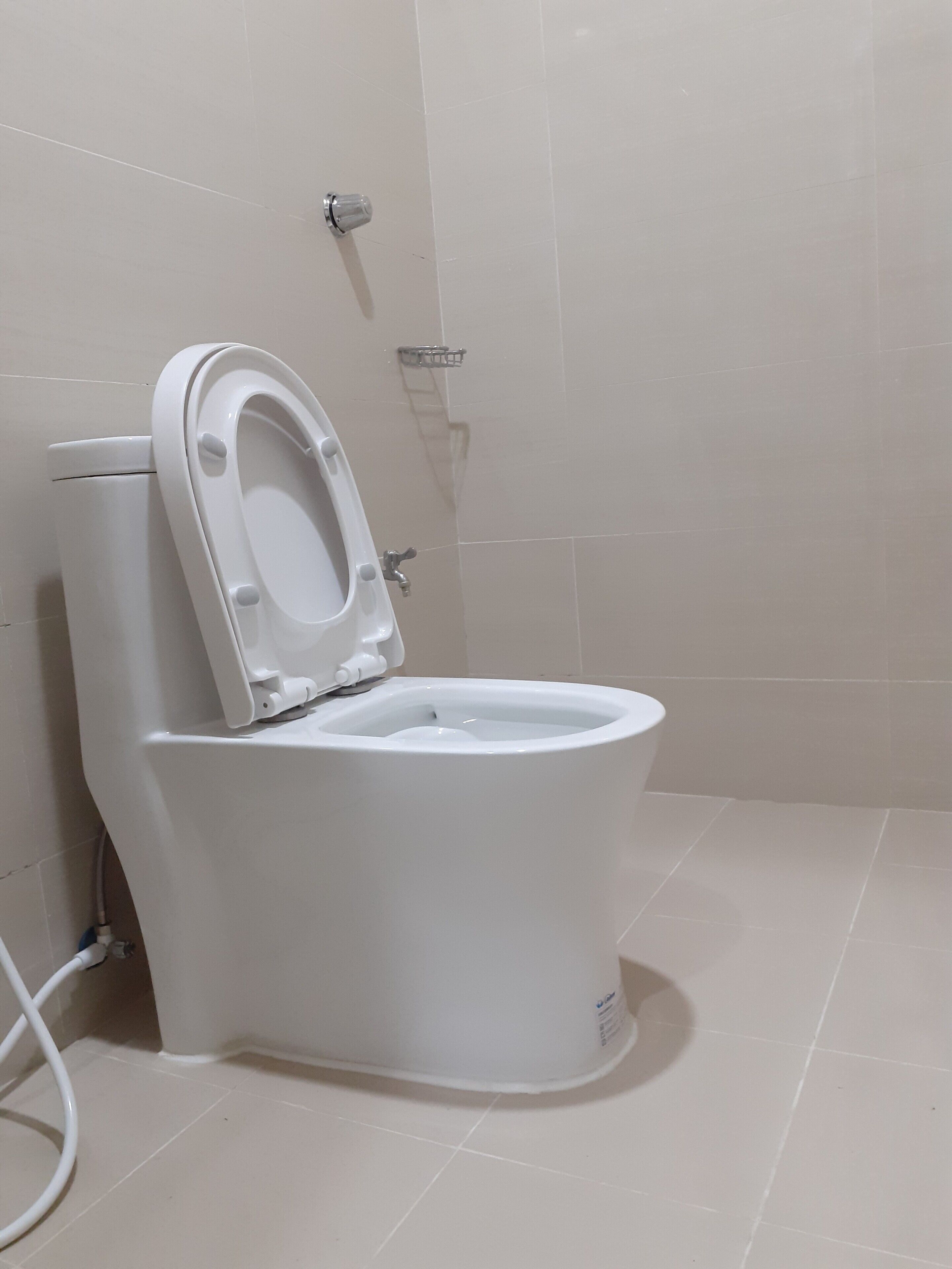 A white toilet in a bathroom with a tiled floor and a shower area in the background.