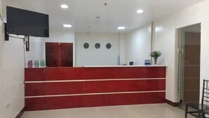 Un espace d’accueil avec un comptoir rouge, un téléviseur à écran plat fixé au mur et une porte.