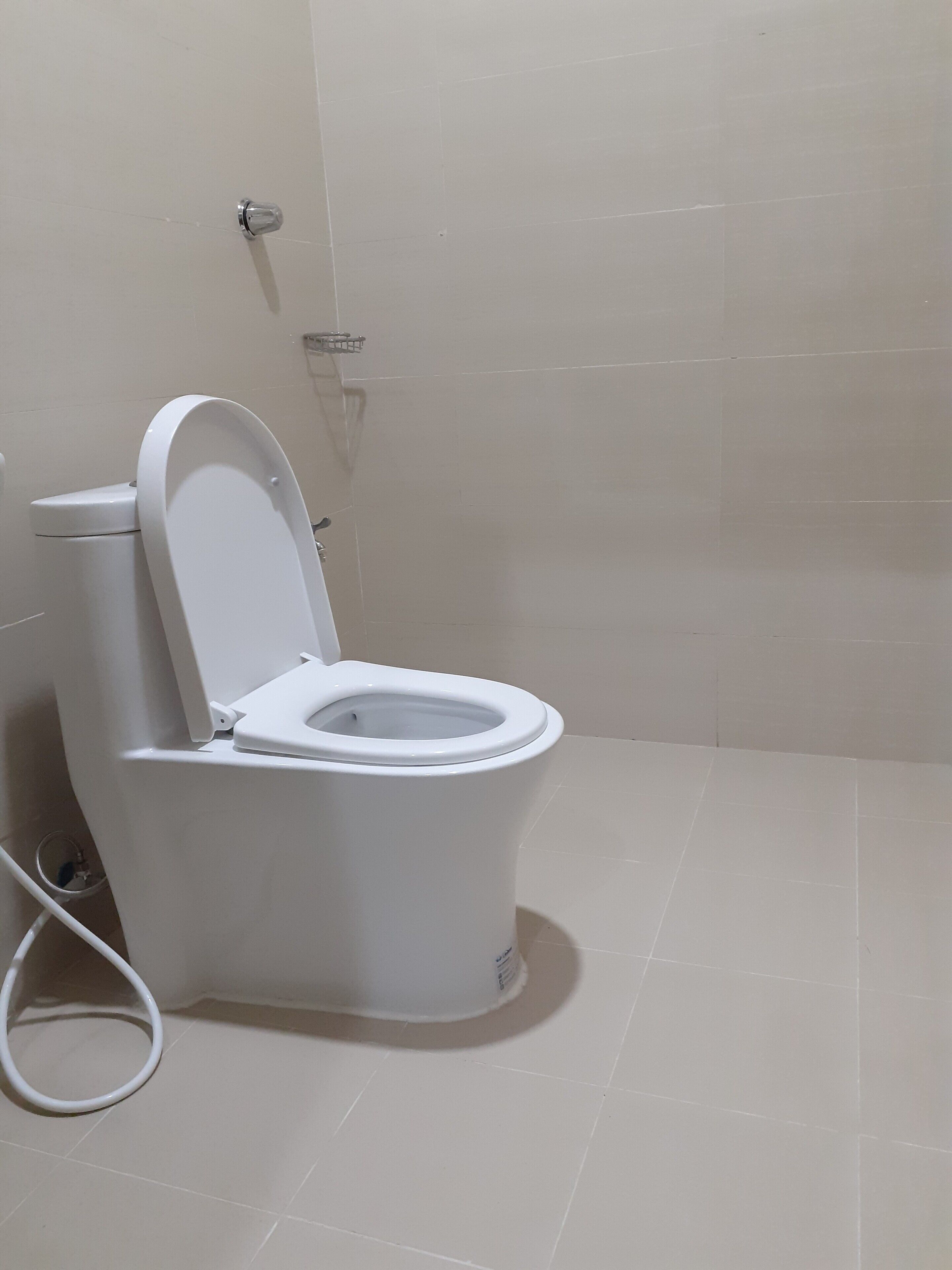 Des toilettes blanches avec un abattant fermé, dans une salle de bain carrelée de carreaux beige.