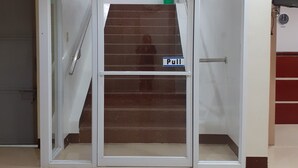 L’entrée d’un hôtel, avec une porte en verre, une poignée pour ouvrir et un escalier menant à l’étage supérieur.