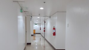 Un couloir propre et bien éclairé, avec des murs blancs, un sol carrelé et du matériel de sécurité incendie.