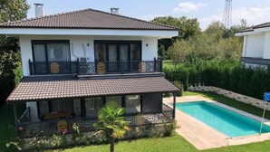 Una casa de dos pisos con balcón, piscina y un jardín bien cuidado.