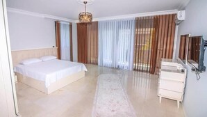 Habitación de hotel con una cama grande, un escritorio, una silla, un espejo, una araña y una ventana con cortinas.